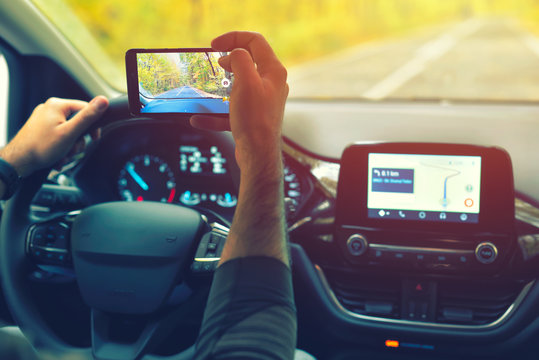 Male driver using smartphone to capture pictures of road, while driving