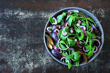 Fresh salad in a bowl. Vegan salad with arugula, plum and blue onion.