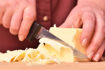 Female hands and knife cut fresh parmesan cheese on a cutting board. Close-up