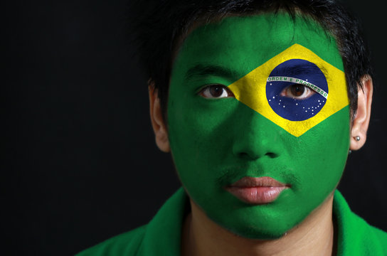 Portrait of a man with the flag of the Brazil painted on his face on black background.