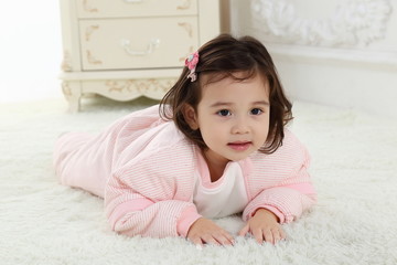 Fototapeta premium the sweet little girl was wearing a pink warm pajamas and smiling on the white carpet