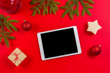 Tablet computer mock up for Christmas time. Fir branches, Christmas decorations and gift box on red background, flat lay top view