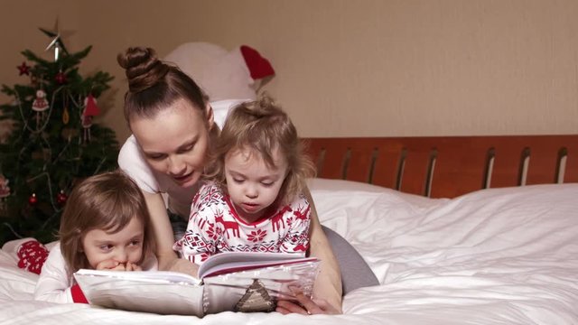 Young mother is reading fairy tales to her small children in the bed in Christmas period