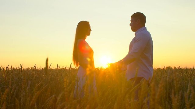 Romantic young happy couple silhouette in golden wheat field at sunset. Woman and man hugging and kissing against shining sun, sun lens flare. Love, happy family, nature, outdoors. Slow motion. 120fps
