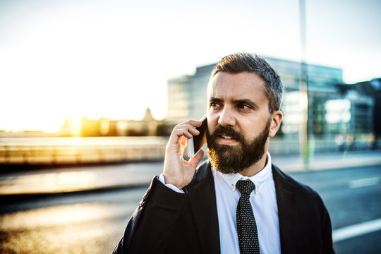 Hipster businessman with smartphone in the city at sunset, making a phone call.
