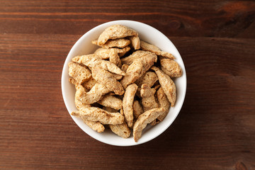 Raw dry soya meat chunks in a white bowl on a wooden table, top view