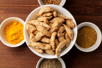 Raw dry soya meat chunks in a white bowl on a wooden table with different species, top view