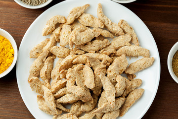 Raw dry soya meat chunks on a white plate on a wooden table with different species