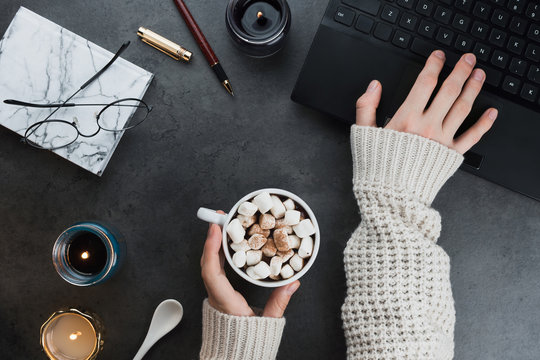 Cozy winter business flatlay arrangement with black laptop, women hands with vegan cocoa and candles on dark marble background