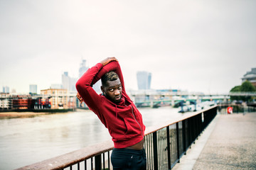 Young sporty black man runner doing stretching on the bridge outside in a city.