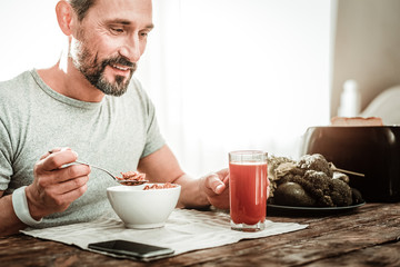 Healthy drink. Joyful positive man taking a glass with juice while eating his breakfast