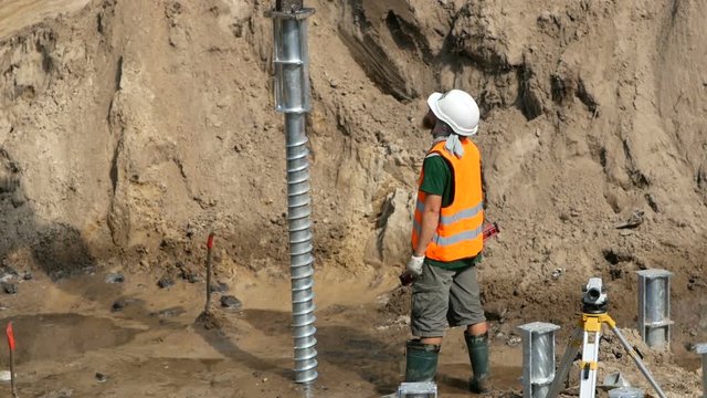 worker controls screwing piles during the construction of an industrial building foundation