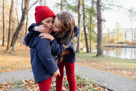 Two happy children hugging and kissing in autumn park. Close up sunny lifestyle fashion portrait of two beautiful caucasian girls outdoors, wearing cute trendy outfit. Sisters relationship