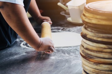 Chef is rolling pin on bread dough for preparing baked pizza homemade