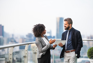 A portrait of two businesspeople with tablet standing against London view panorama.