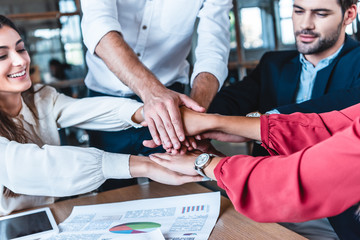 cropped shot fo business team holding hands at workplace in office