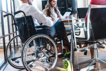cropped shot of young disabled businessman in wheelchair working with colleagues in office