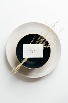 Table setting with a white plate and a black bowl styled with dried grass and a handwritten place card.