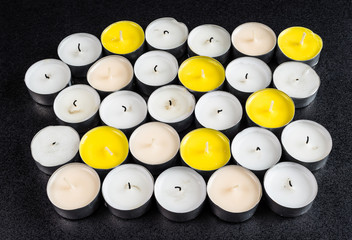 A set of white and yellow tealight paraffin candle lying on a black background.