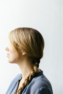 A woman with long dark blond hair tied up in a braid looking towards the light seen en profil from the side.