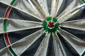 Darts in a dartboard. 3 darts in a bulls eye.