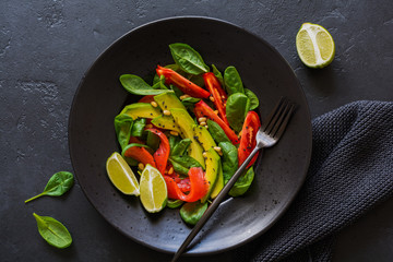 Avocado, salmon, spinach, tomato, pine nuts and black sesame salad in a black ceramic plate. Top view.