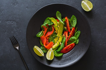 Avocado, salmon, spinach, tomato, pine nuts and black sesame salad in a black ceramic plate. Top view.