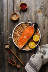 Steaks of chum salmon raw with spices, herbs, salt and lemon on old wooden background. Top view copy space.
