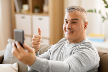 Obraz premium technology, people and communication concept - happy man having video chat on smartphone at home and showing thumbs up