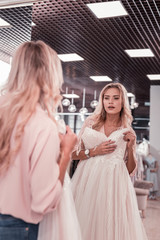 Is it beautiful. Pleasant young woman standing in front of the mirror while checking the wedding dress