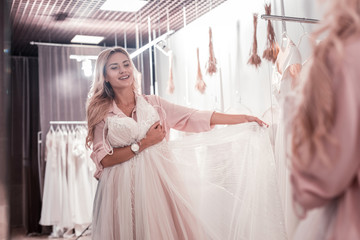 So beautiful. Positive attractive woman holding a wedding dress while imagining herself a bride