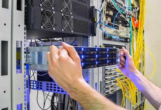 Installation of a new server in a rack with computer equipment. Performing work to replace the server in the data center. The system administrator's hands hold a powerful supercomputer.