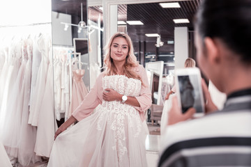 Naklejka premium Great picture. Delighted joyful woman smiling while posing for a photo with a wedding dress