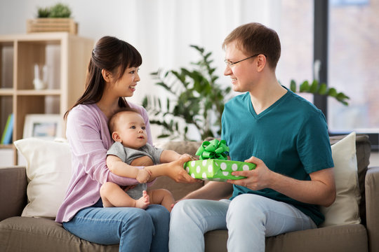 family, parenthood and fathers day concept - happy mother with baby boy giving birthday present to father at home