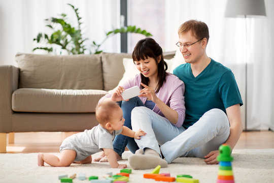 family, technology and people concept - happy mother and father taking picture or recording video of baby boy with smartphone at home