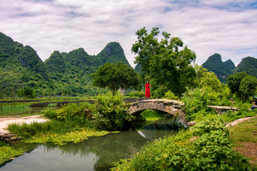 Girl in red dress stand in the old stone bridge