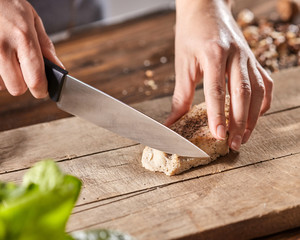 A woman's hands are cutting meat on a wooden board on an old wooden table. Step-by-step cooking