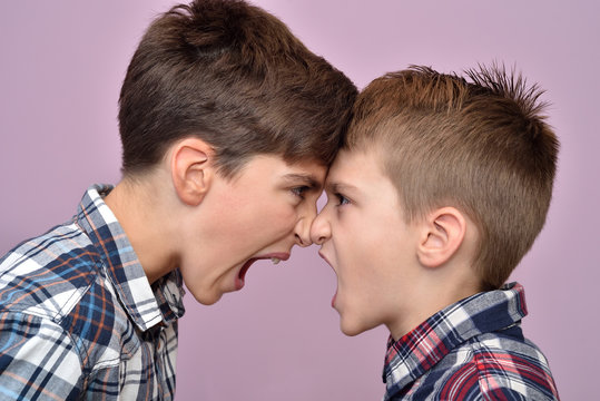 Two angry brothers standing face to face, quarreling, shouting and looking at each other
