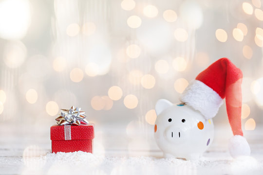 Red santa hat with piggy bank and present on bokeh light background.