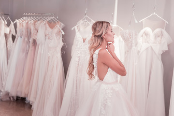 Wedding dress salon. Positive young woman looking at the wedding dresses while being in the wedding...