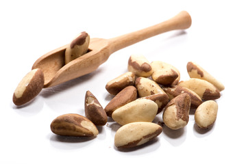 Close-up of pile of roasted, salted brazil nuts in a wooden spoon on white background