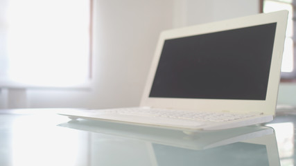 Fototapeta premium Place of work, laptop opened and blank screen on modern table with morning light in white color room, blurred image for business blurred image for business office concepts