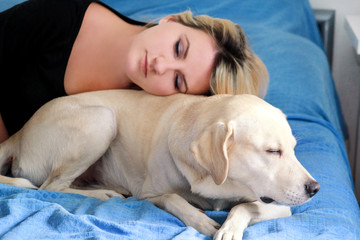 Obraz premium Woman with cute dogs at home. Handsome girl resting and sleeping with her dog in bed in bedroom. Owner and dog sleeping in sofa. Yellow labrador retriever relax. Portrait of woman and her best friend.