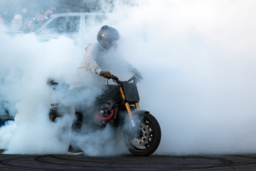 Biker staying on the motorcycle, burning tire and creating smoke on the bike show