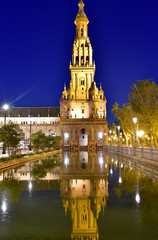 Fototapeta na wymiar Tower reflected in water basin, illuminated Plaza de Espana, night view, Seville, Andalusia, Spain