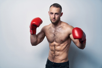 Muscular shirtless man wearing box gloves ready to struggle, looking at camera