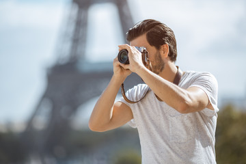 Paris Eiffel Tower tourist with camera taking pictures in front of the Eiffel tower, Paris, France. Young professional photographer handsome man in casual clothes outdoors in Europe.