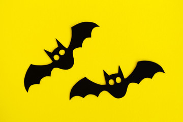 Holiday decorations for Halloween. Two black paper bats on a yellow background, top view.
