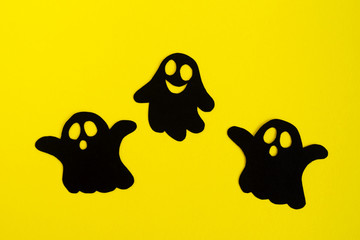 Holiday decorations for Halloween. Three black paper ghosts on a yellow background, top view.
