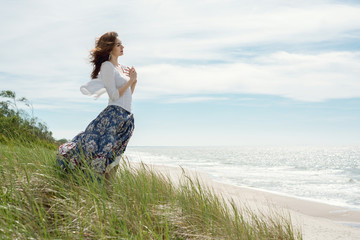Young brunette woman in dress stands by the sea